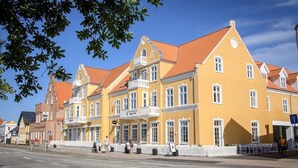 A yellow building with a red roof, multiple windows, and a white fence in front.