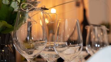 Una fila de copas de vino vacías sobre una mesa, con una planta y una vela al fondo.