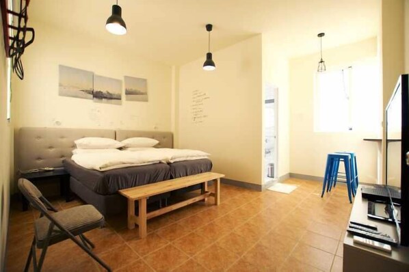 A bedroom with a bed, bedside tables, a bench, a chair, and a desk with a computer.