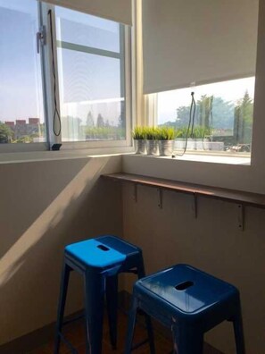 A room with a window overlooking a cityscape, two blue stools, and a shelf with potted plants. - LP Guesthouse (Taitung)