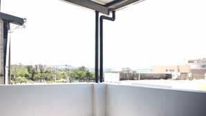 Un balcón con una mesa de madera y un cubo de metal, con vista a una zona residencial con árboles y edificios.