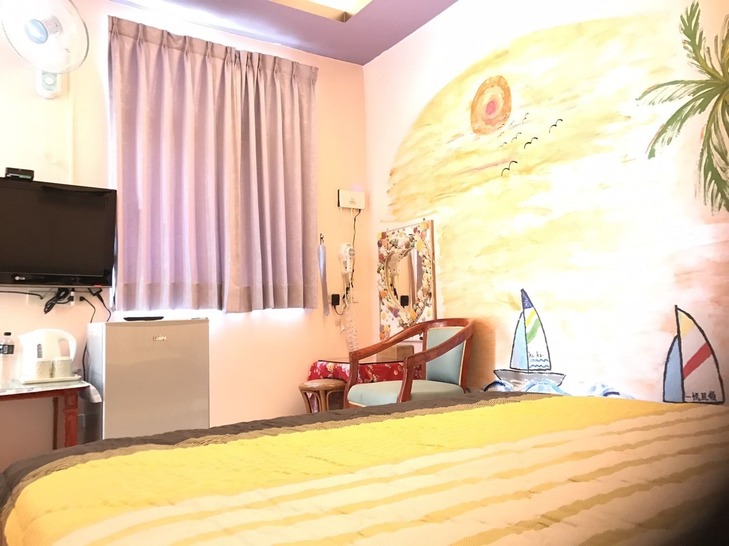 Una habitación de hotel con una cama, un televisor, un escritorio con una computadora, una silla, una mesita con una botella y un cuadro de un planeta en la pared.