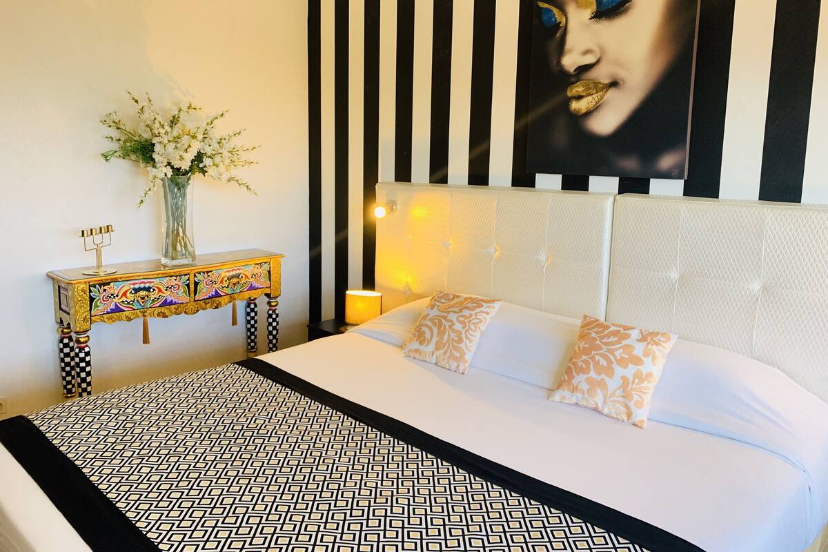 Een hotelkamer met een bed, een nachtkastje, een decoratieve vaas en een kunstwerk aan de muur.