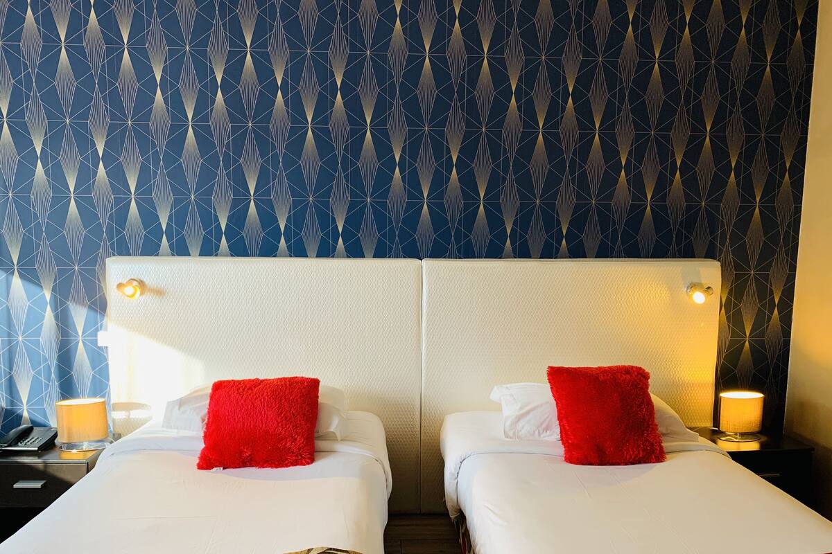 Een hotelkamer met twee bedden, elk met een witte hoofdbord en rode kussens. De kamer heeft behang met een patroon en bedlampen.