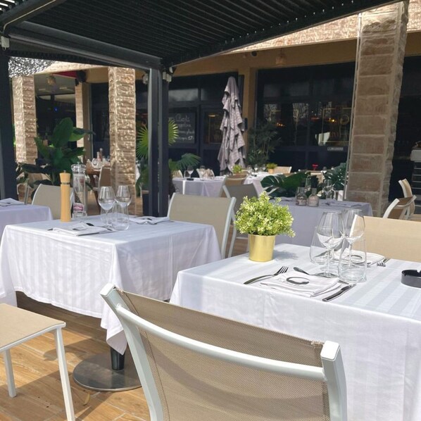 An outdoor dining area with tables set for two, covered by white canopies, and surrounded by brick pillars. - Grand Hôtel de Nîmes (Nîmes)