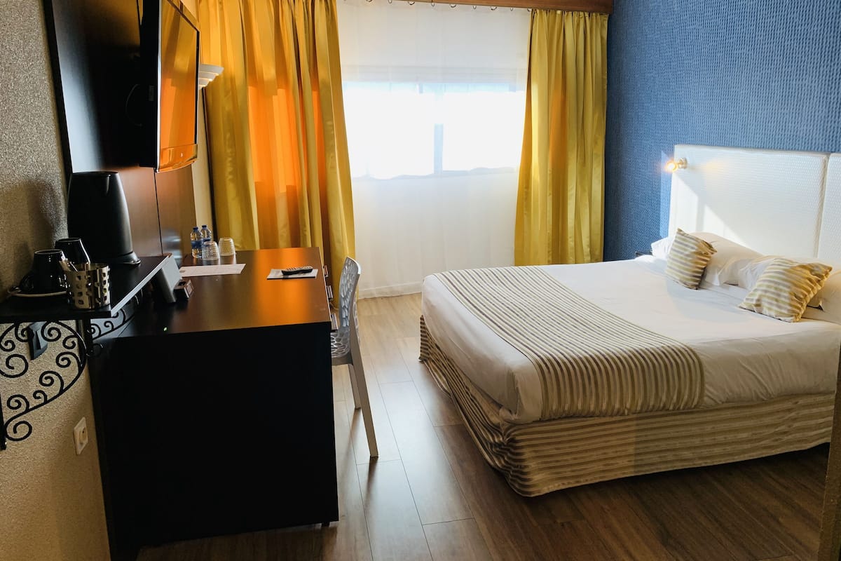 Een hotelkamer met een bed, een bureau, een televisie en gordijnen.