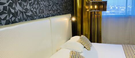 A hotel room with a geometric patterned wall, a large window with curtains, and a bed with striped pillows.