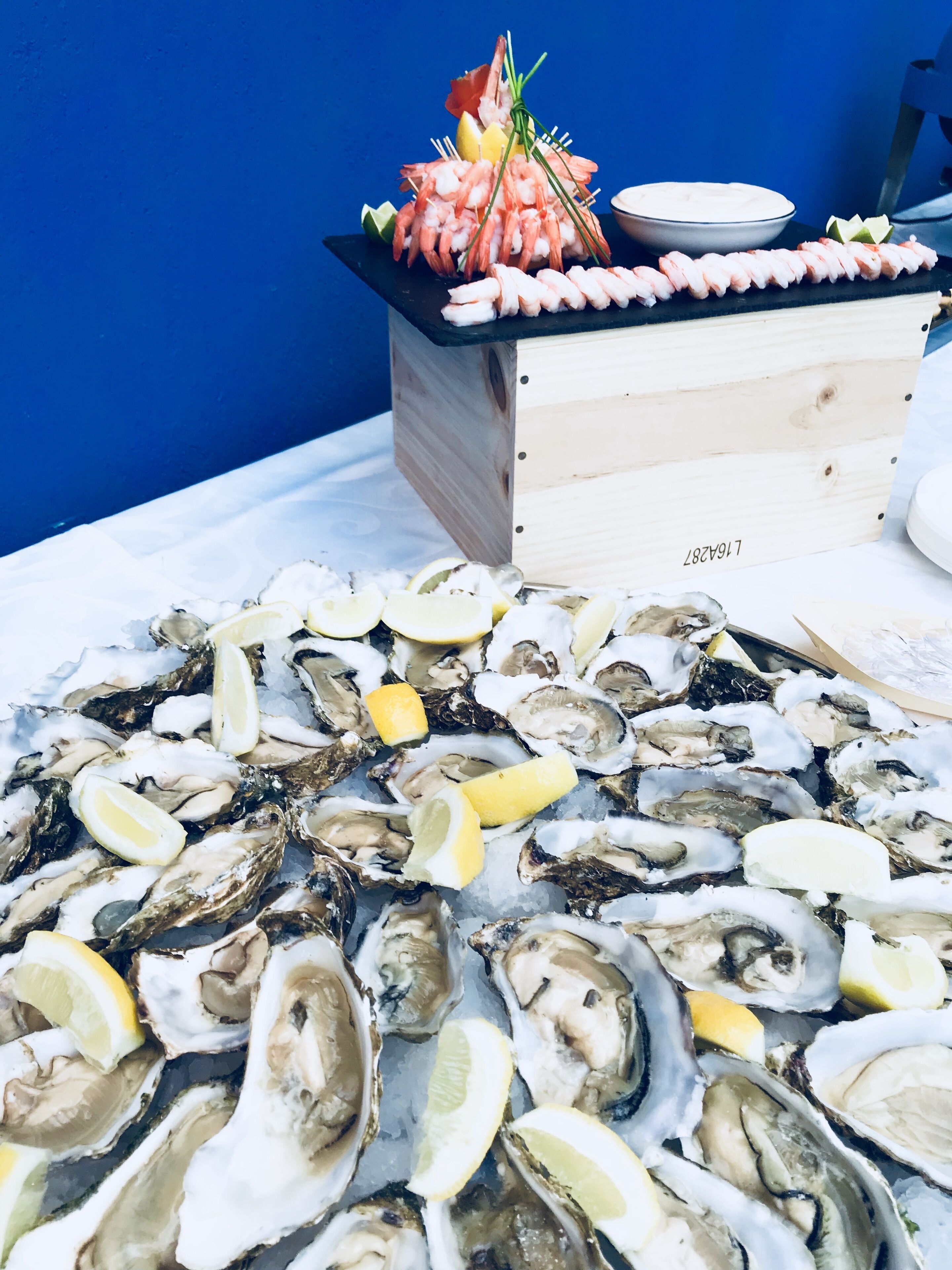 Exhibición de mariscos con ostras y camarones sobre hielo, acompañada de gajos de limón y un cuenco de salsa.