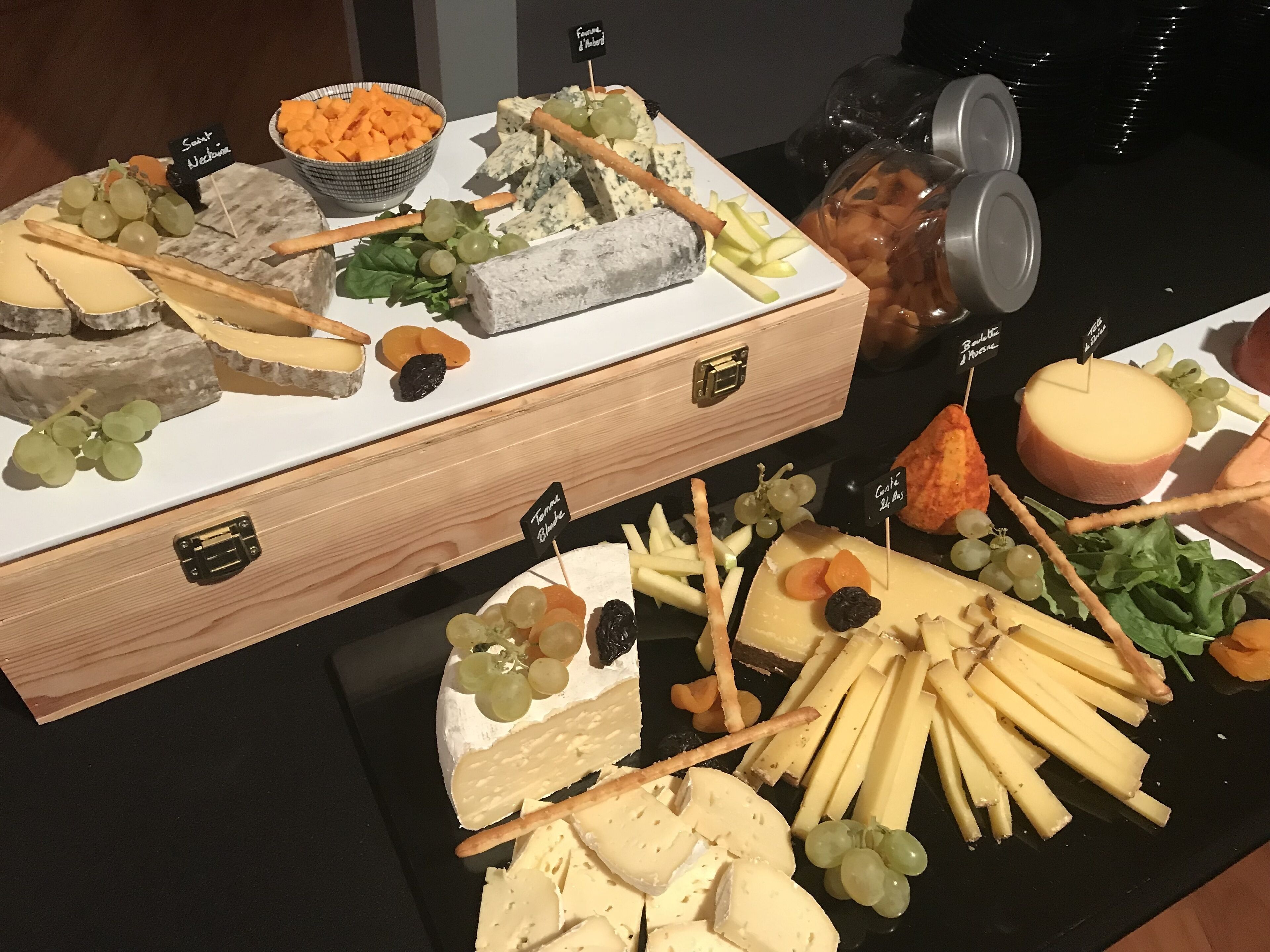 Un plateau de fromages et de fruits comprenant différents types de fromages, des raisins et des crackers.