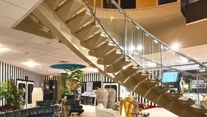 Een ruime lobby met een moderne trap, zwarte leren banken, een witte fauteuil en decoratieve gouden beeldjes van dieren.