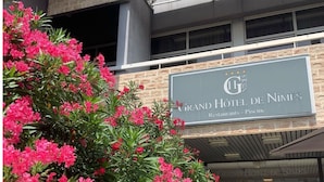 Het uiterlijk van het Grand Hotel de Nimes, met een bord waarop staat dat er restaurants en een pizzeria zijn.
