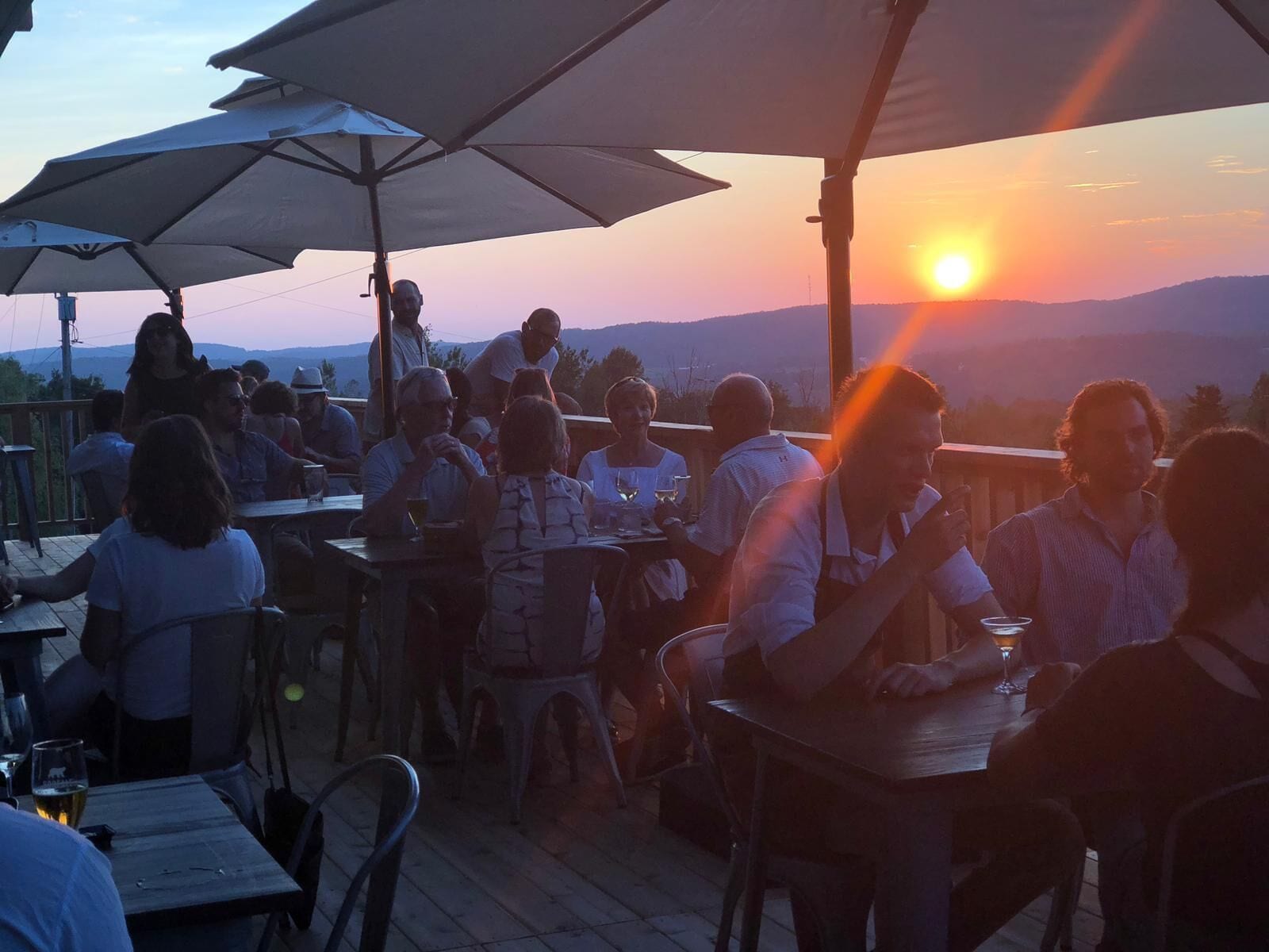 Area esterna con tavoli e sedie, ombrelloni e vista sul tramonto su un paesaggio collinare.