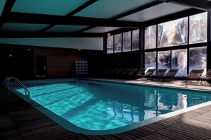 An indoor swimming pool with clear water, surrounded by lounge chairs and large windows. - Hotel Horizon (Sutton)