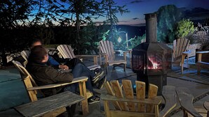A wooden deck with Adirondack chairs, a wood-burning stove, and a person sitting on a chair. - Hotel Horizon (Sutton)