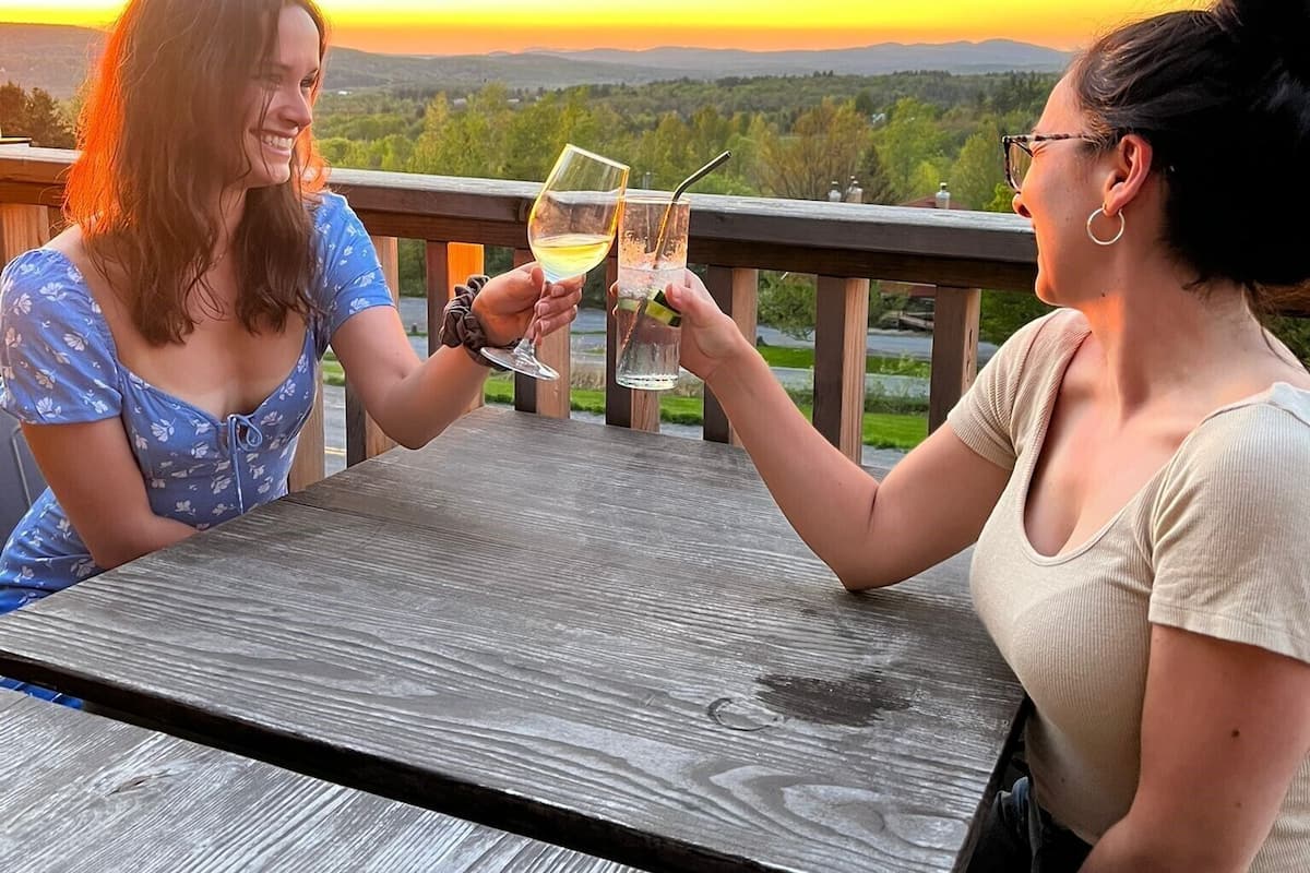 Deux personnes trinquent autour d’une table en bois, avec un paysage magnifique en arrière-plan.