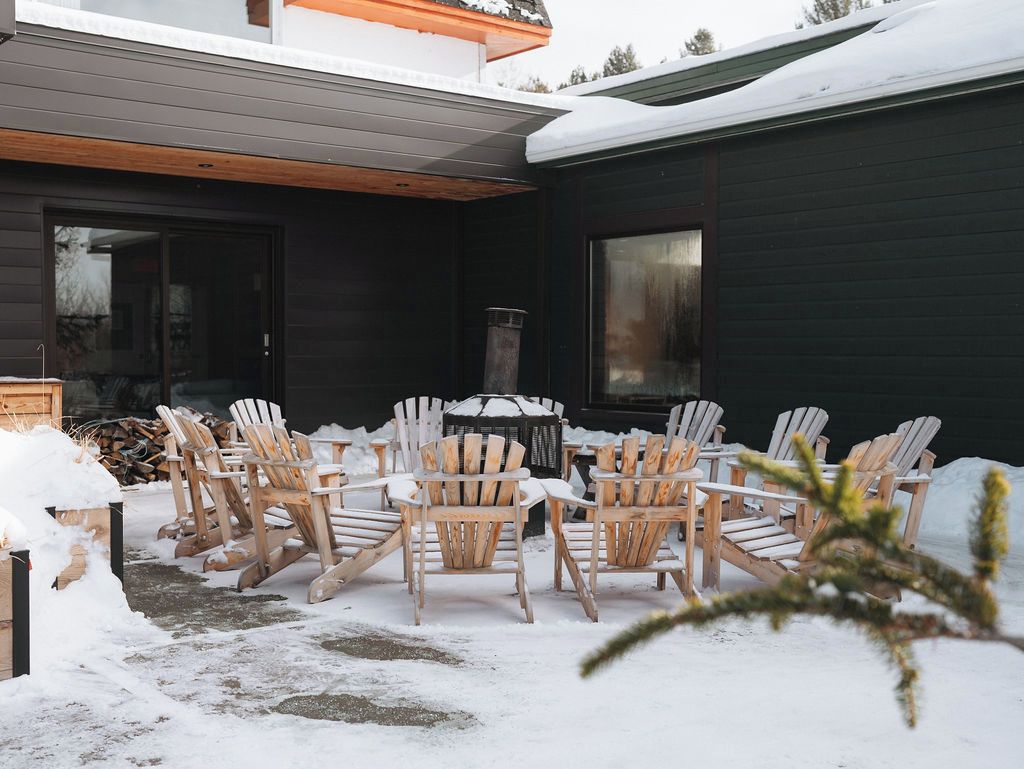An outdoor seating area with wooden chairs and tables, a fire pit, and a snow-covered ground.
