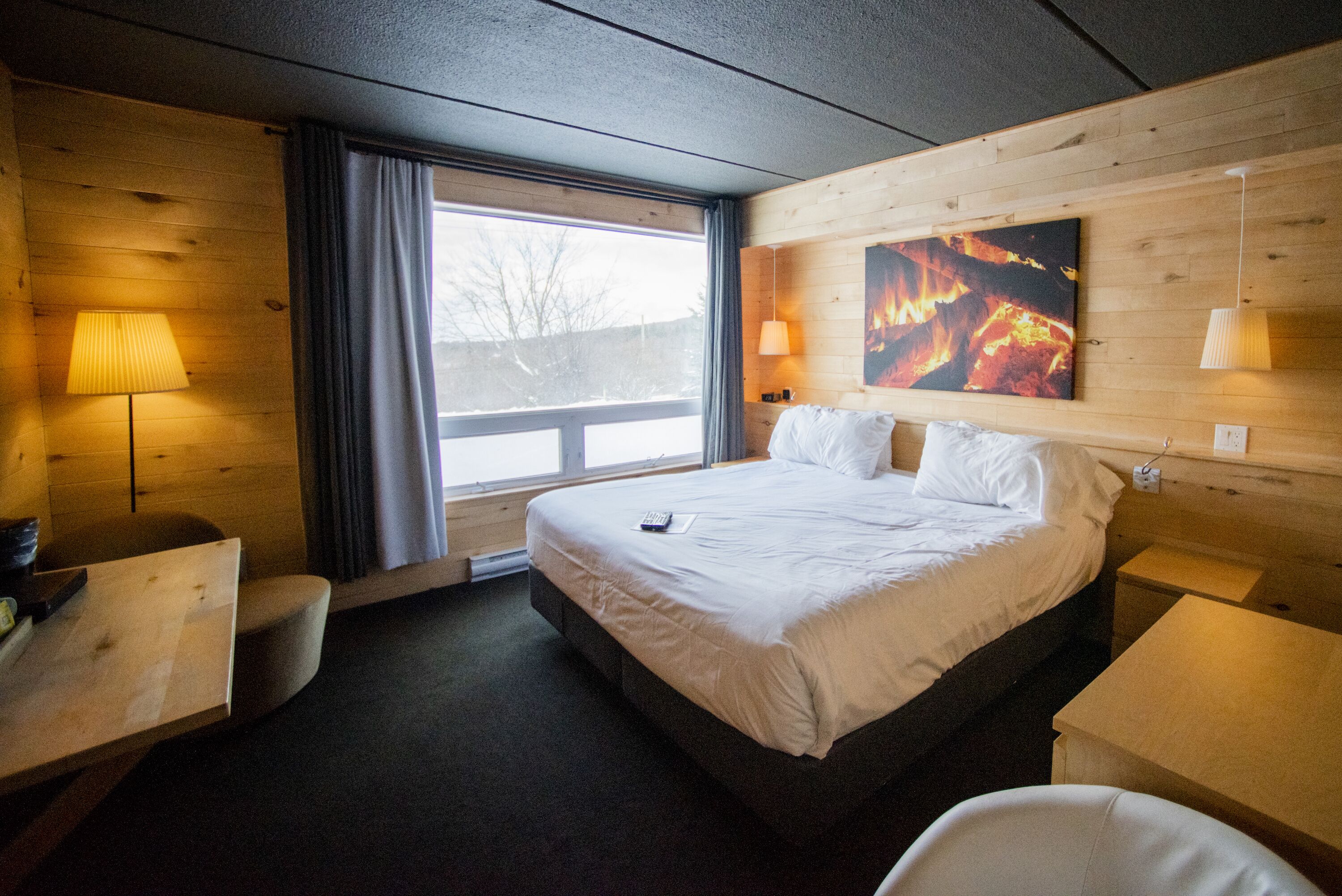Ein Hotelzimmer mit einem großen Bett, einem Schreibtisch, einem Sessel, einer Lampe und einem Wandbild mit Feuer.