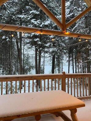 A wooden bench on a balcony with a view of a snowy forest. - Hotel Horizon (Sutton)