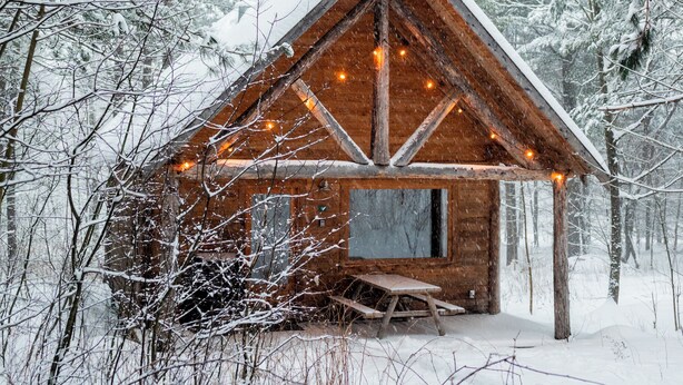 A wooden cabin with a triangular roof, surrounded by snow-covered trees. - Hotel Horizon (Sutton)