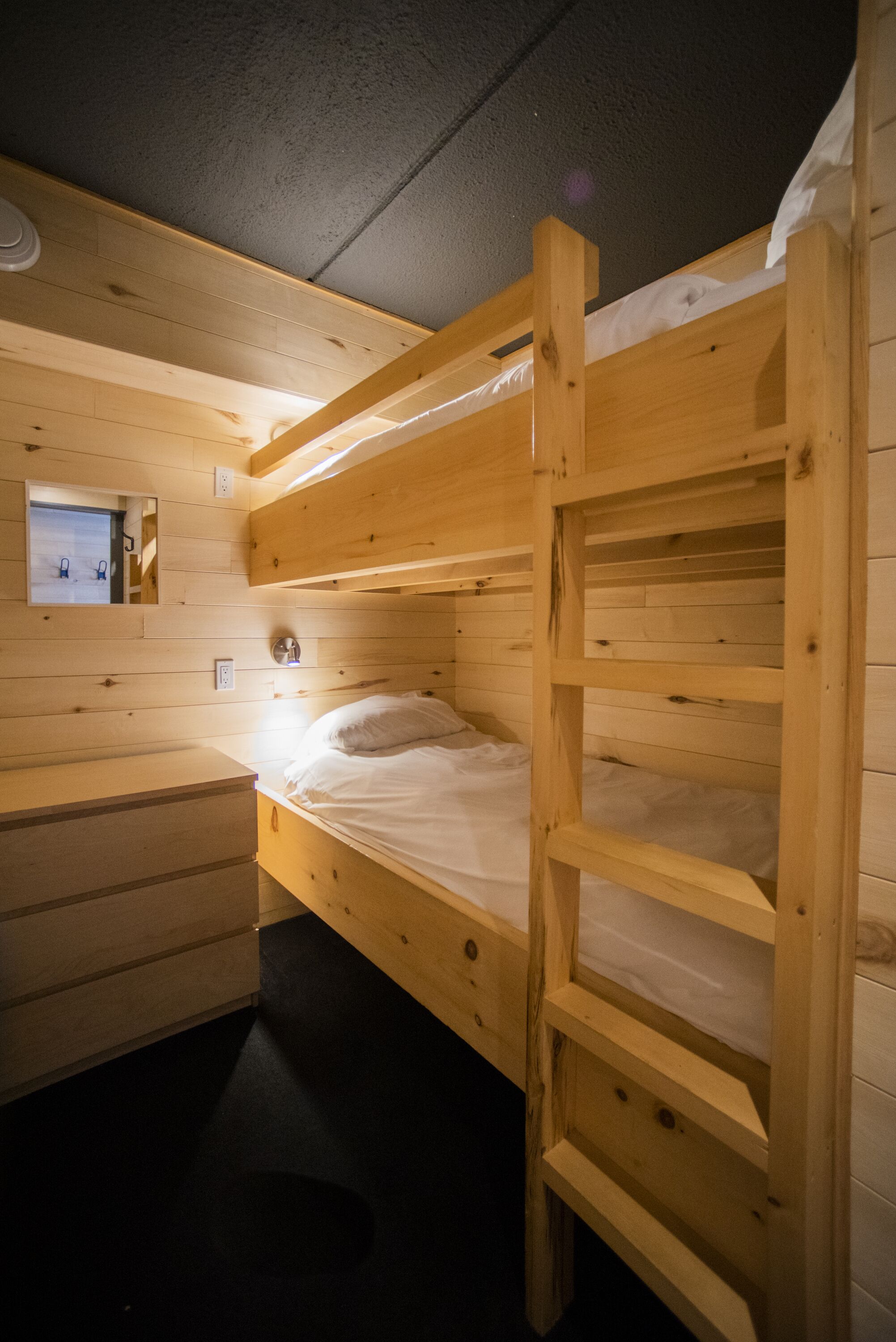 A bunk bed room with wooden walls, a small window, and a bedside table.