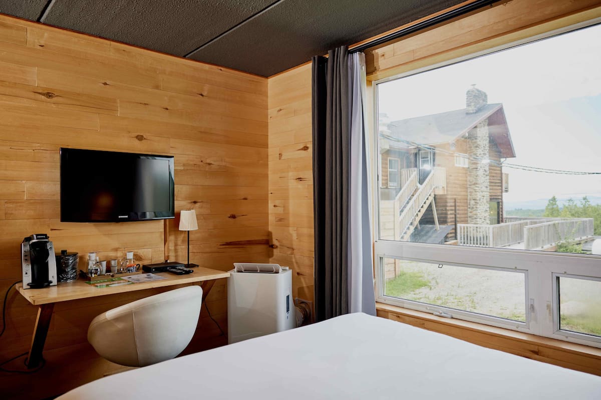 Une pièce aux murs lambrissés, comprenant un lit, un bureau et un téléviseur.