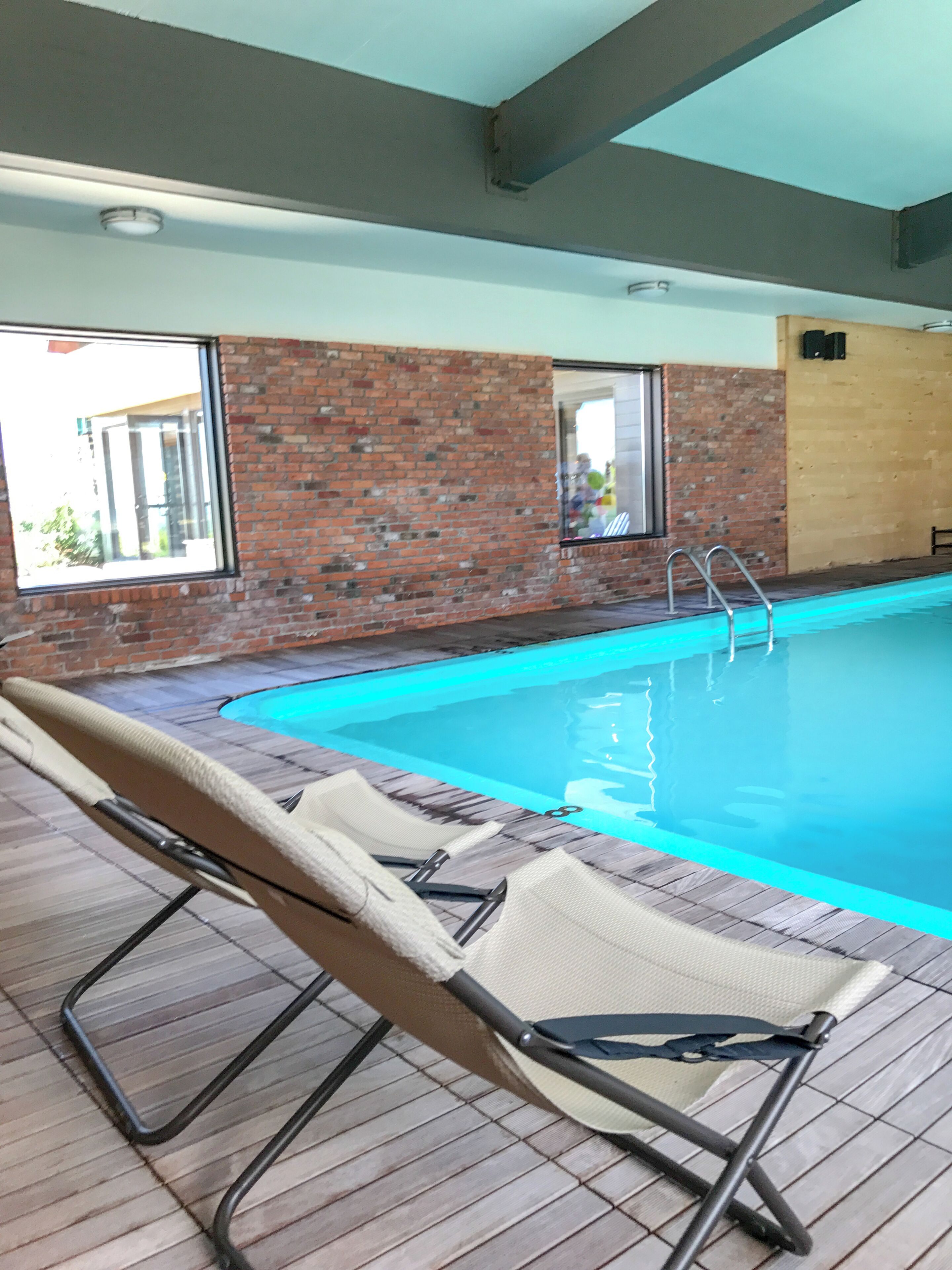 An indoor swimming pool with lounge chairs, a brick wall, and a window.