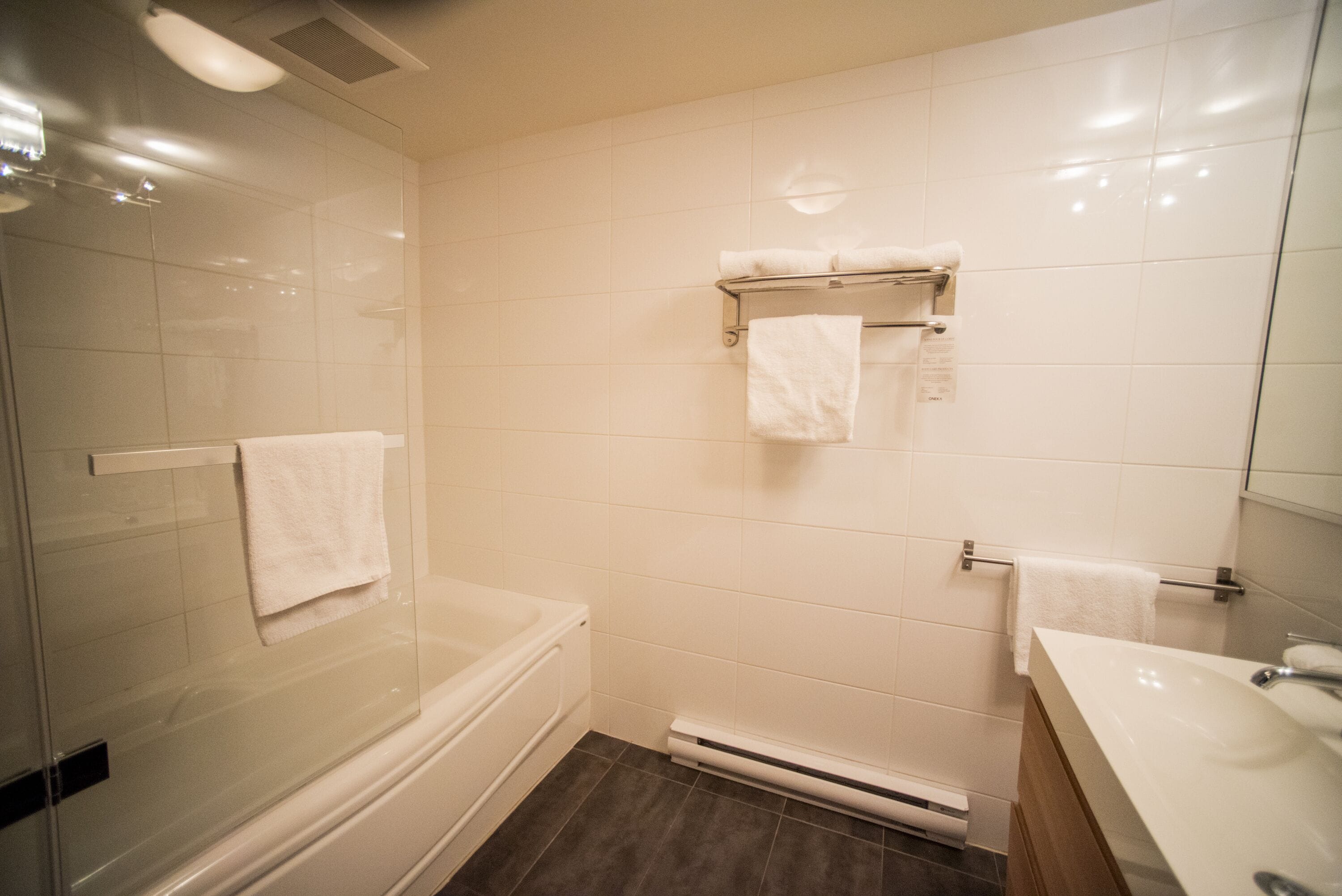 Un baño moderno con ducha de vidrio, bañera, lavamanos integrado y un perchero con dos toallas.