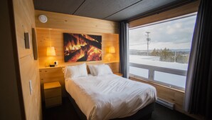 A hotel room with a bed, bedside lamps, a painting on the wall, and a window with a view of a snowy landscape. - Hotel Horizon (Sutton)