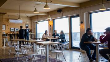 A cafe with wooden tables and chairs, large windows, and hanging pendant lights.