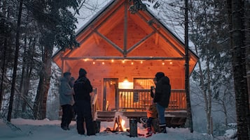 A wooden cabin with a porch, surrounded by snow-covered trees.