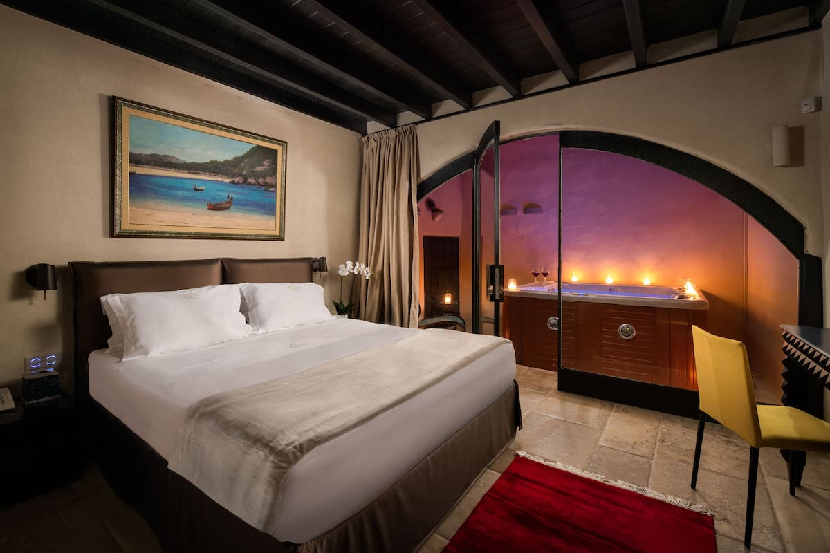 A hotel room with a large bed, a painting of a beach scene, a vanity with a mirror, and a red rug.