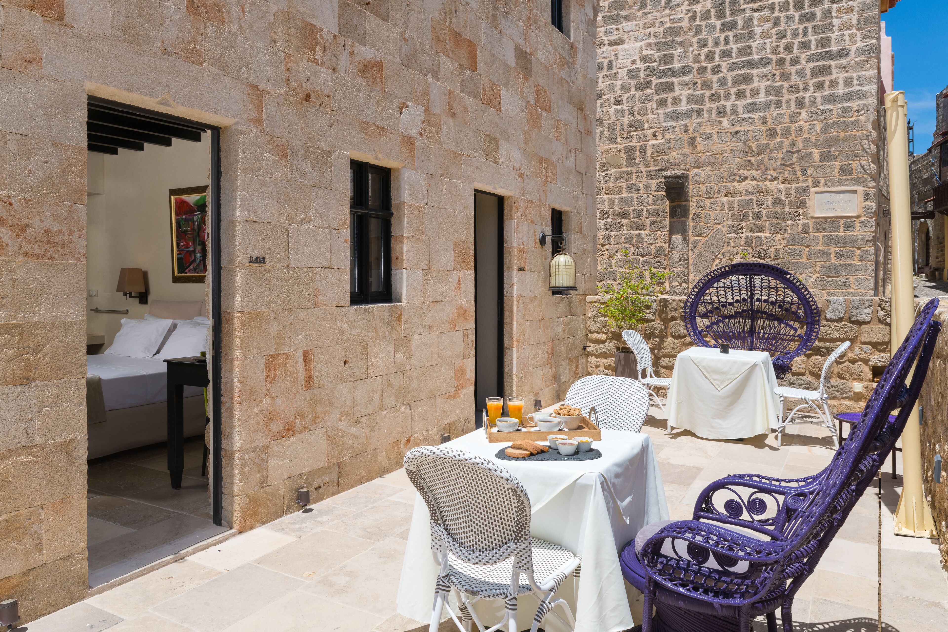 A stone building with a dining area featuring wicker chairs and a table set for breakfast.
