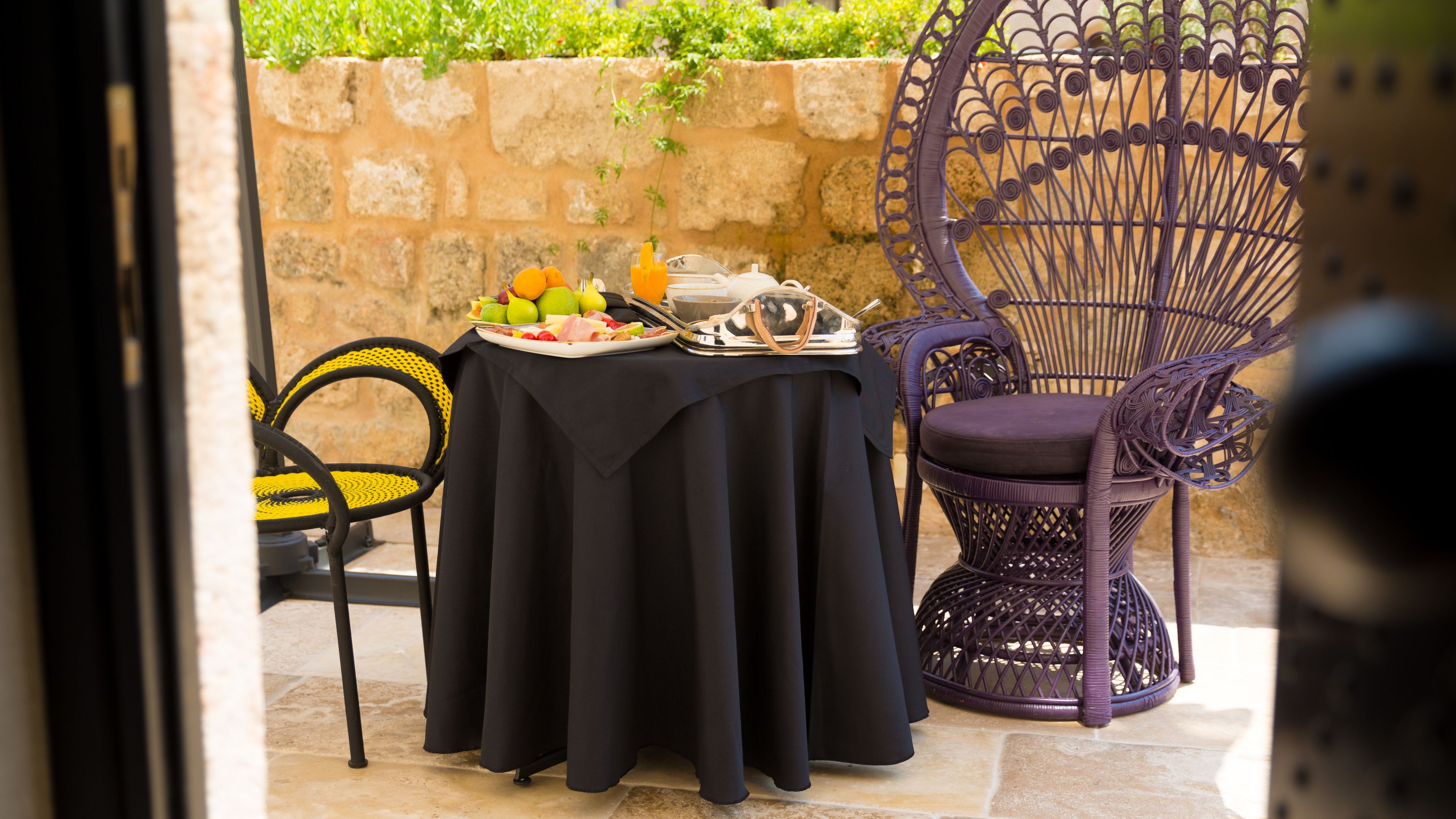 An outdoor dining area with a table set for two, featuring a black tablecloth, a wicker chair, and a metal chair.