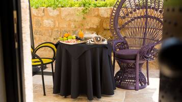 An outdoor dining area with a table set for two, featuring a black tablecloth, a wicker chair, and a metal chair.
