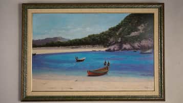 A framed painting of a beach scene with boats and a mountain in the background.