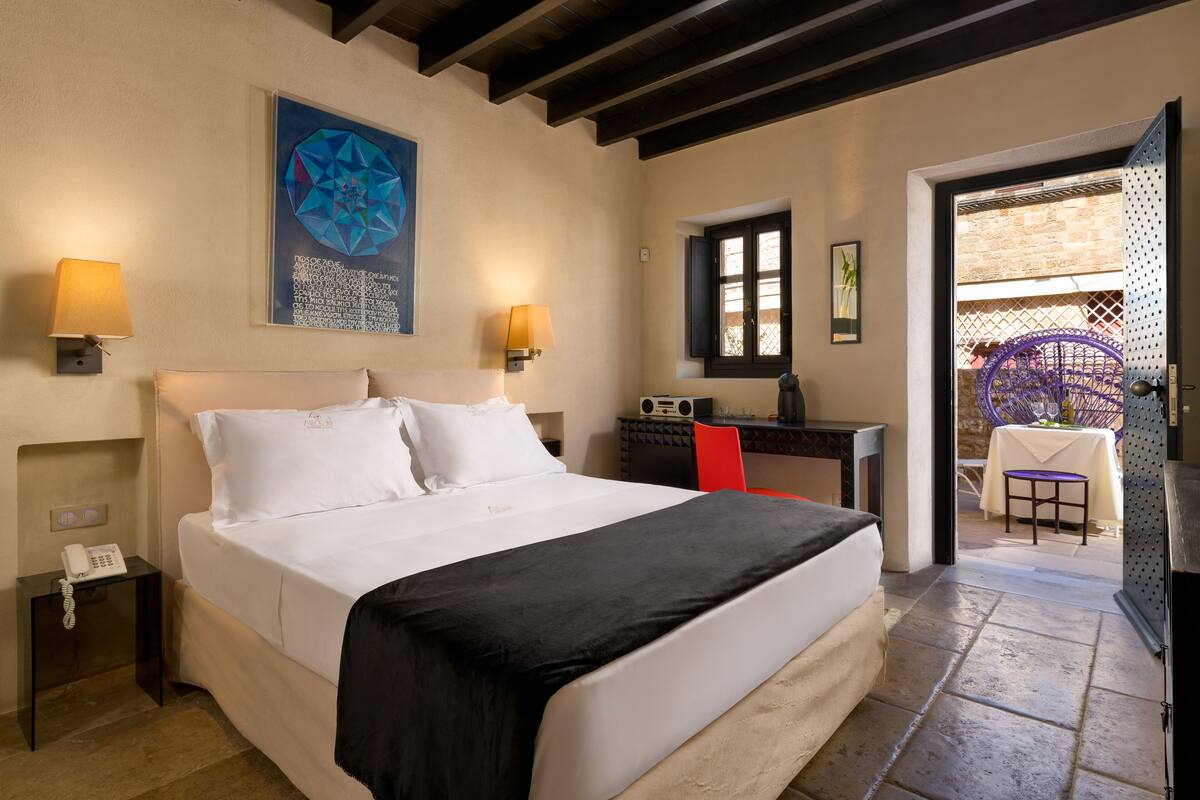 A hotel room with a large bed, two bedside lamps, a desk with a chair, and a view of the outside.