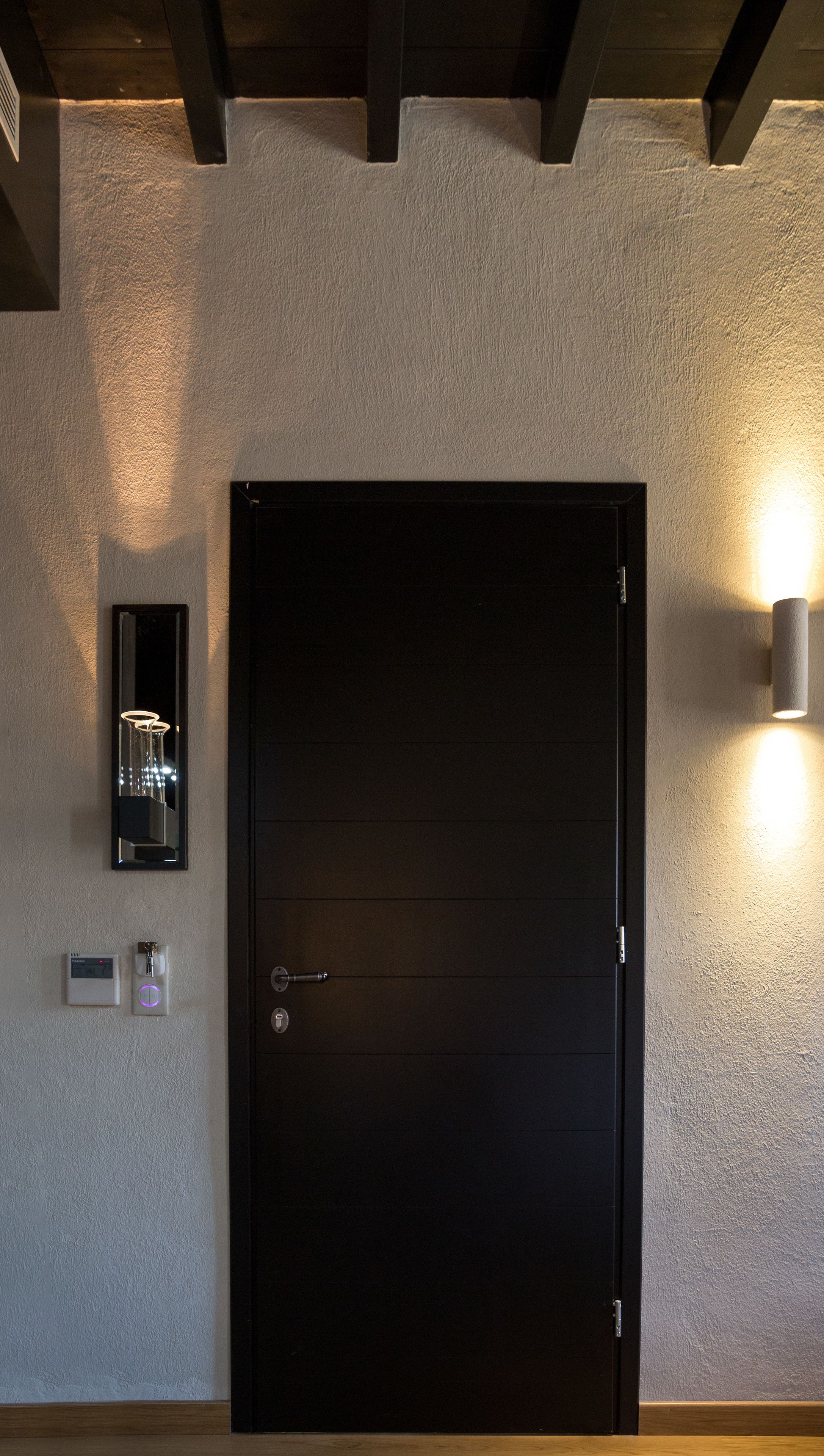 A black door with a handle, a wall-mounted light fixture, and a thermostat on the wall.