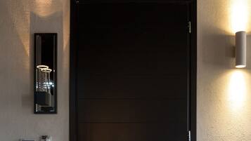A black door with a handle, a wall-mounted light fixture, and a thermostat on the wall.