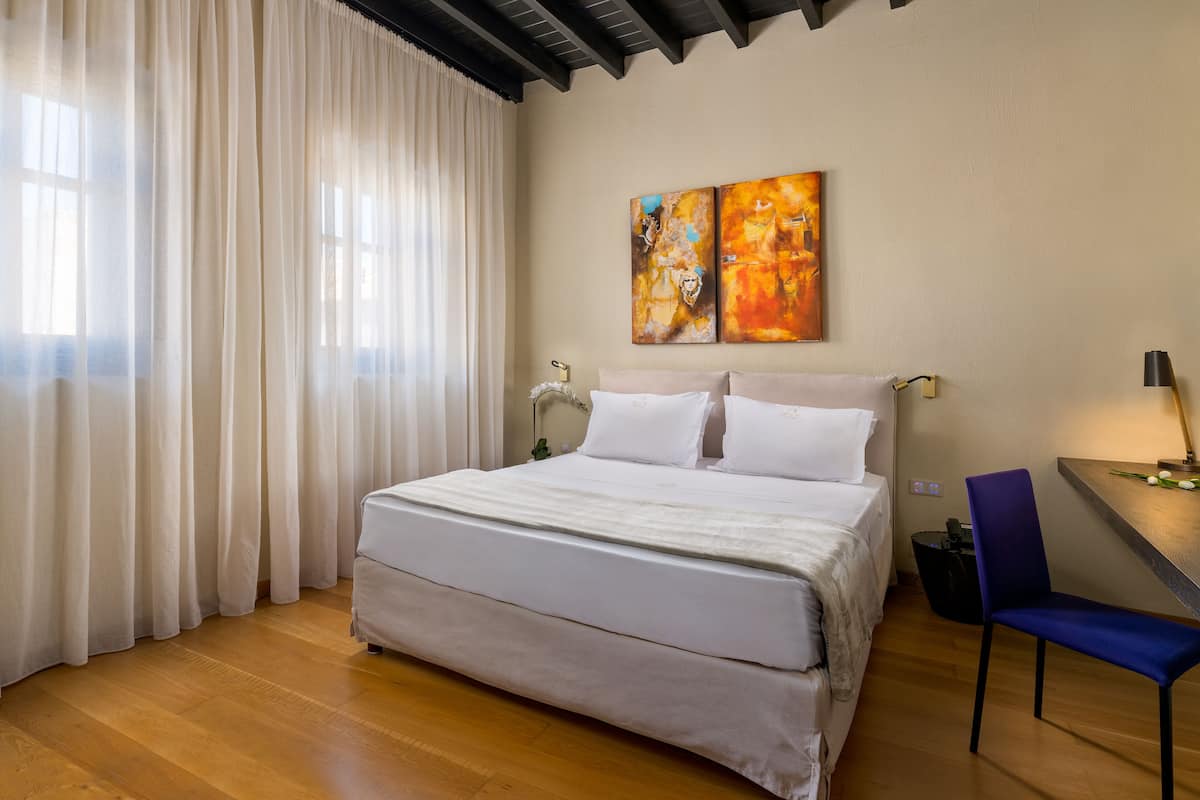 A bedroom with a bed, a desk, a chair, and two paintings on the wall.