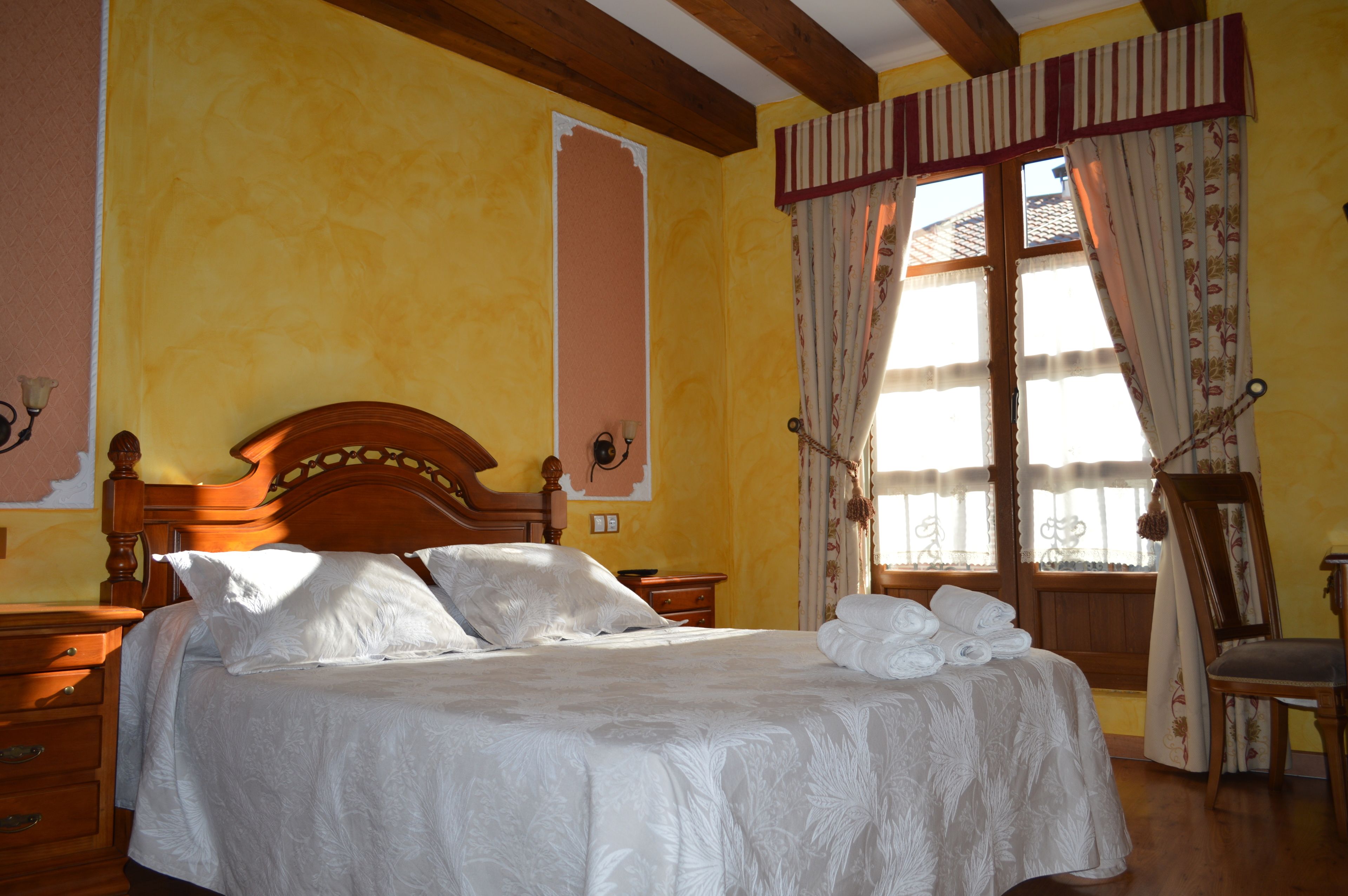 Un dormitorio con una cama de madera, una mesita de noche, una silla y una ventana con cortinas.