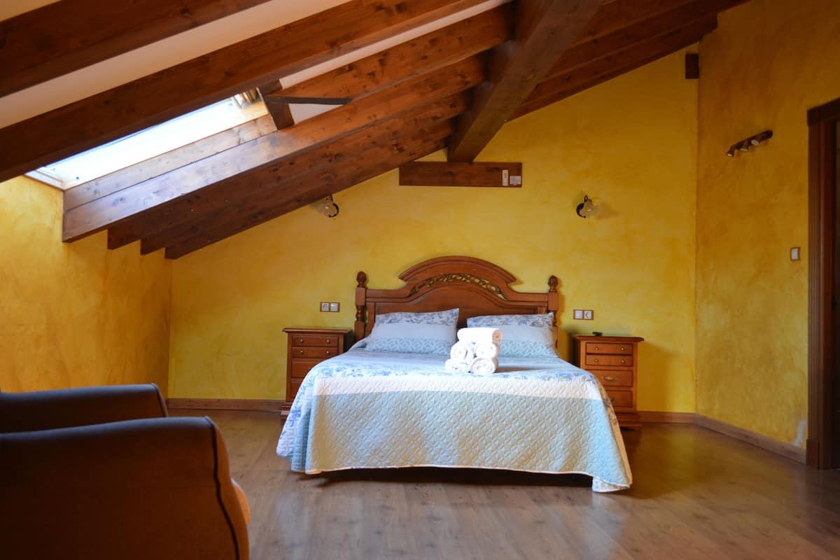 A bedroom with a wooden ceiling, a bed with a quilt, two bedside tables, and a nightstand.