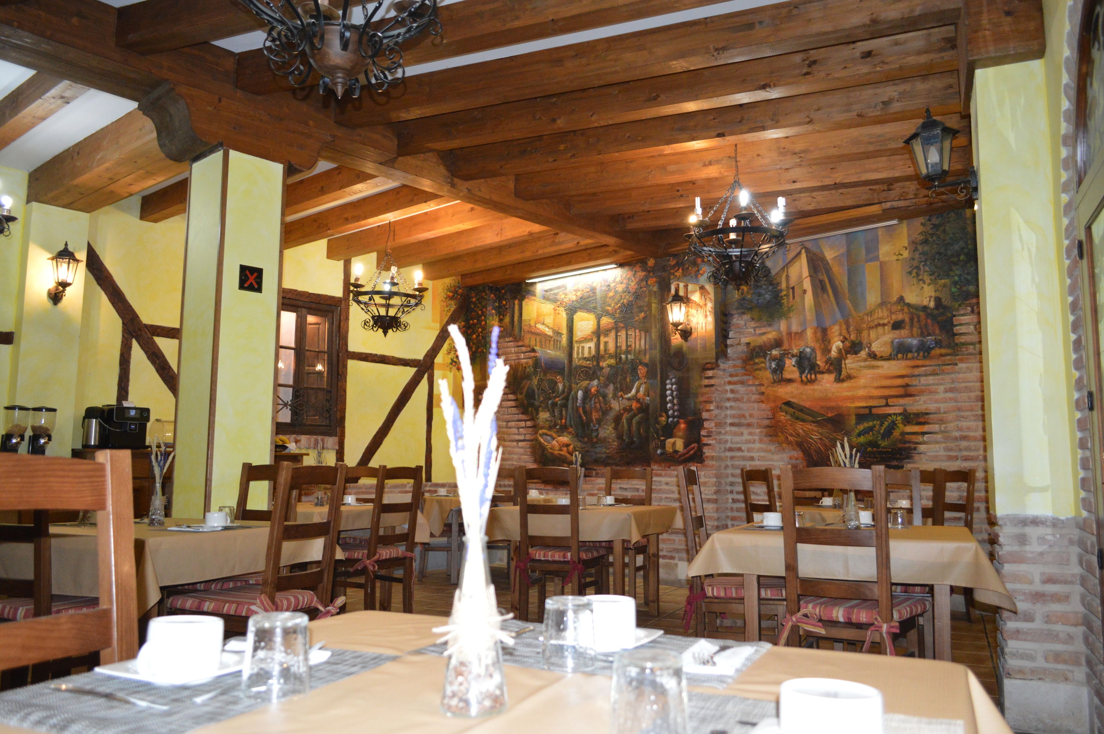 A restaurant with wooden beams, brick walls, and a mural. Tables are set with white tablecloths and candles.