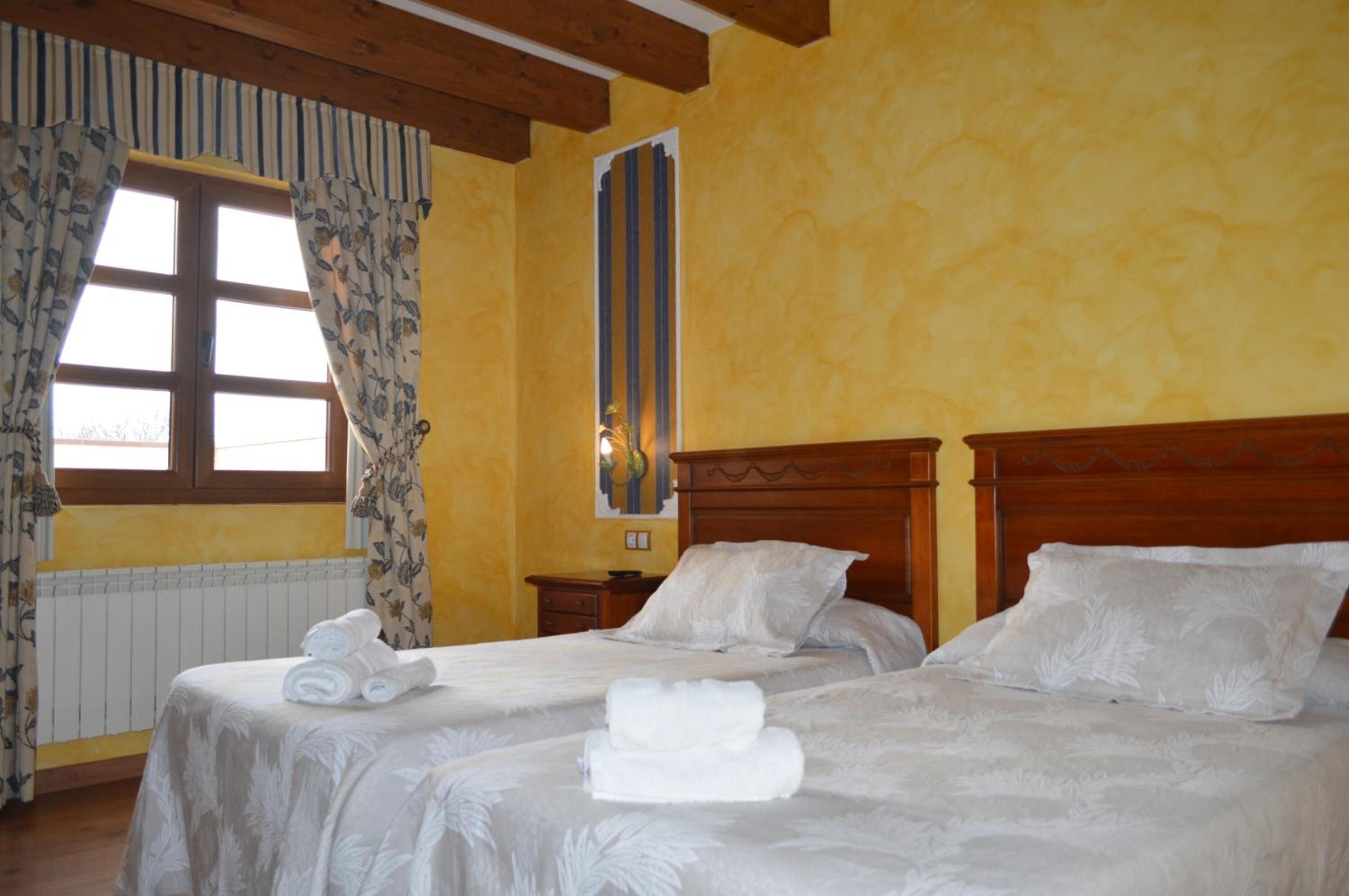 Habitación de hotel con dos camas, cabeceros de madera y una ventana con cortinas.