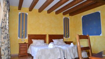 Una habitación con dos camas, cabeceros de madera, un aparador de madera y un ventanal con cortina azul estampada.