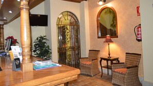 Un vestíbulo con mostrador de recepción de madera, sillas de mimbre, un espejo decorativo y un televisor montado en la pared.