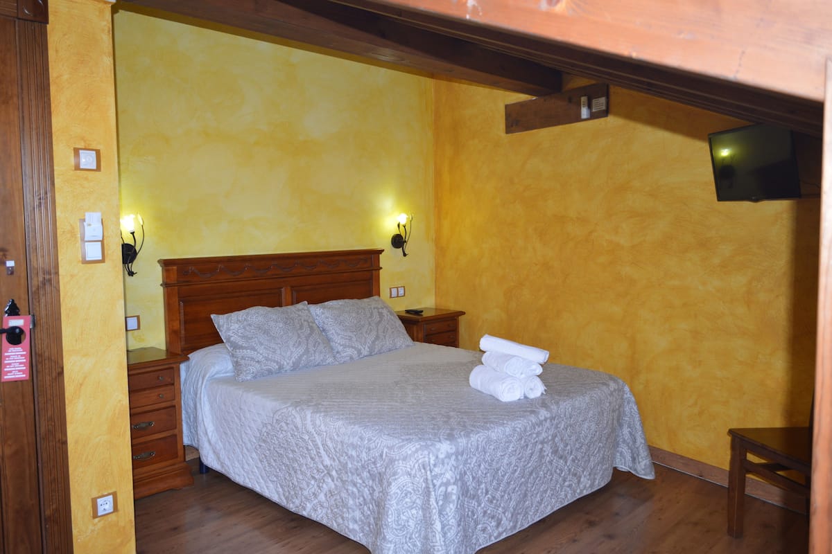 A single bed with a wooden headboard, two bedside lamps, and a small table to the right.