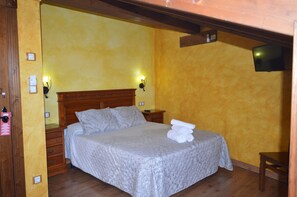 Una cama individual con cabecera de madera, dos lámparas de noche y una mesita a la derecha.