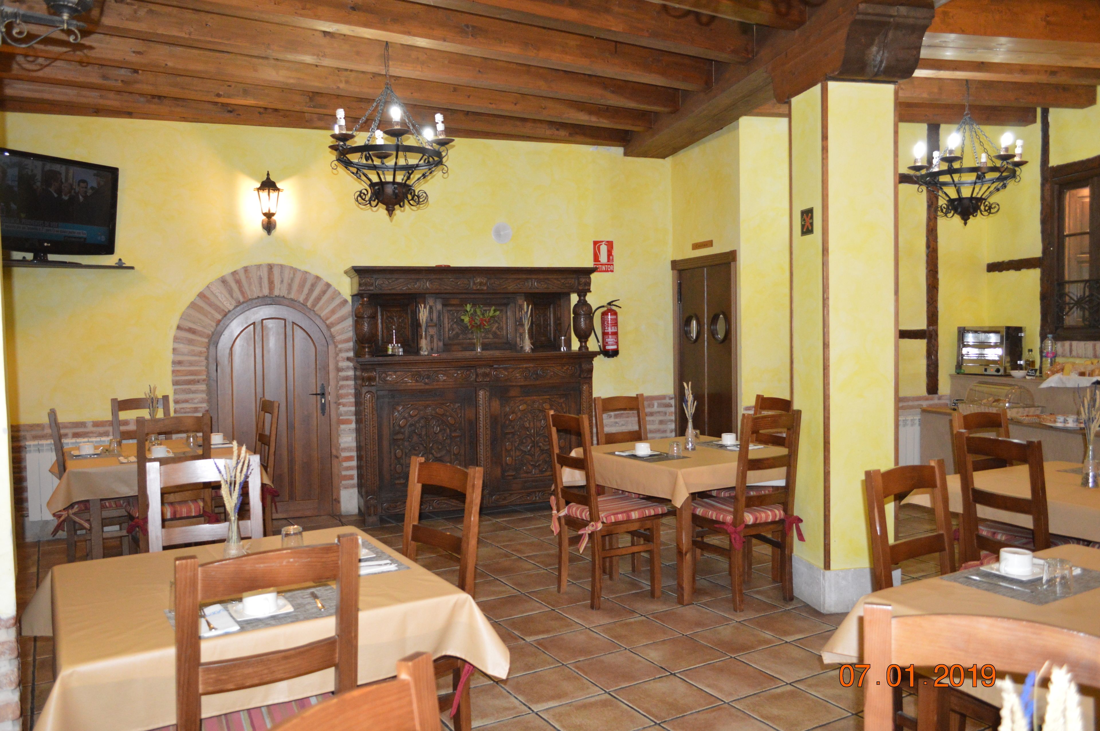 A restaurant with wooden tables and chairs, a brick fireplace, and hanging light fixtures.