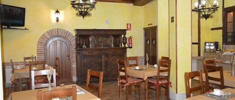 A restaurant with wooden tables and chairs, a brick fireplace, and hanging light fixtures.