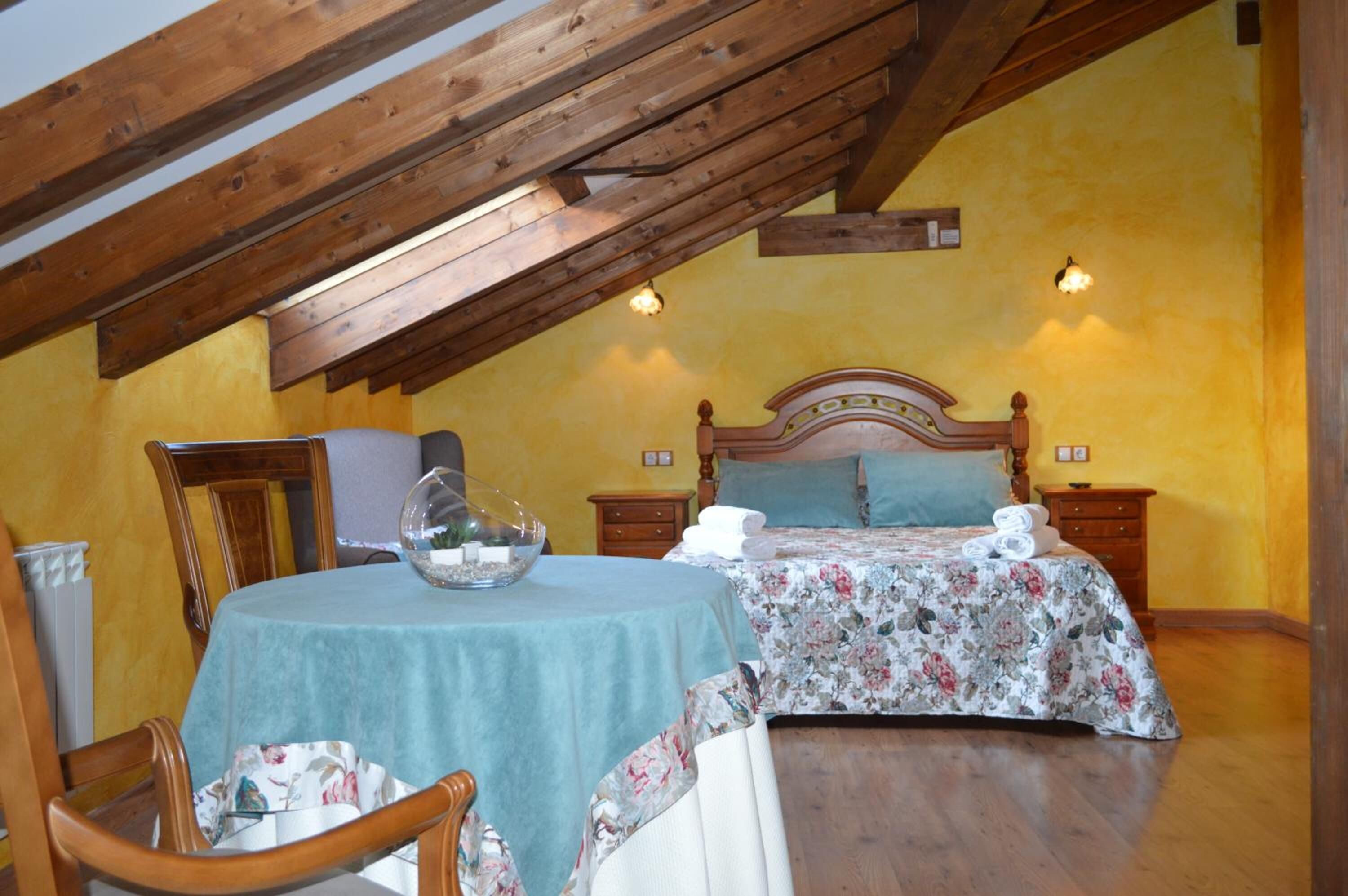 Un dormitorio con techo de madera, una cama con ropa de cama floral, una mesa con mantel azul y dos lámparas de noche.